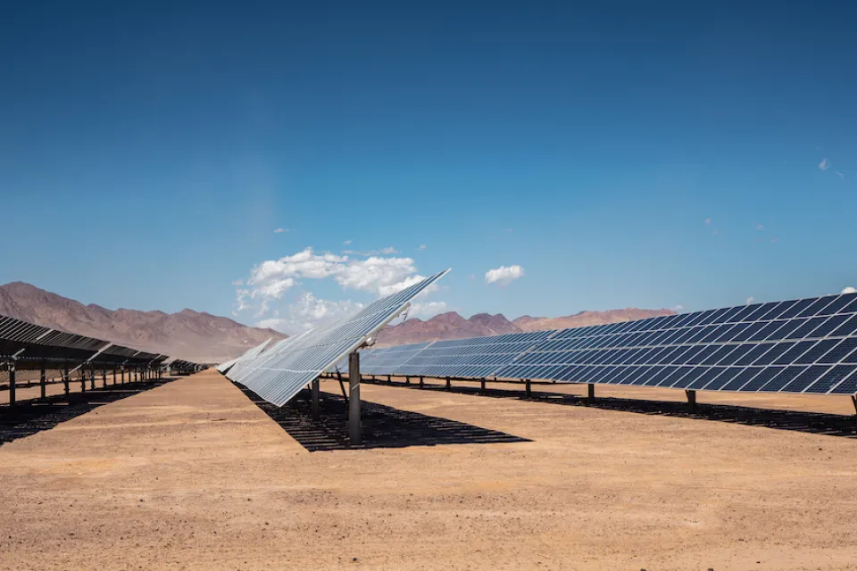 Rows of photovoltaic solar panels in the Nevada desert with mountains in background.